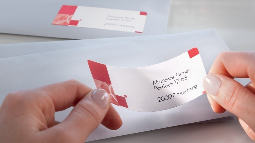 Dvije ruke lijepe pravokutnu adresnu naljepnicu na bijelu omotnicu; na naljepnici se nalazi ime i prezime primatelja, adresa poštanskog pretinca i grad Hamburg, a u pozadini leži još jedna adresirana omotnica