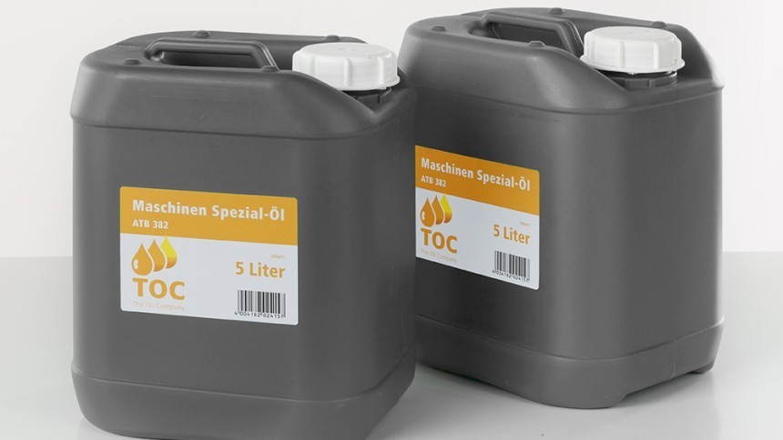 Dva siva plastična kanistera s bijelim čepovima, postavljena na bijeloj pozadini. Svaki kanister ima žuto-bijelu etiketu s natpisom 'Maschinen Spezial-Öl 5 Liter', logotipom s kapljicama ulja i crtičnim kodom.