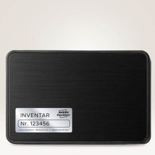 Srebrna inventarska naljepnica Avery Zweckform s brojem ‘Br. 123456’ zalijepljena na crnom metalnom kućištu uređaja