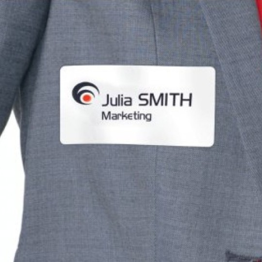 Bijela identifikacijska oznaka s otisnutim logotipom tvrtke, imenom i odjelom „Marketing” pričvršćena je na sivoj jakni preko crvene košulje.