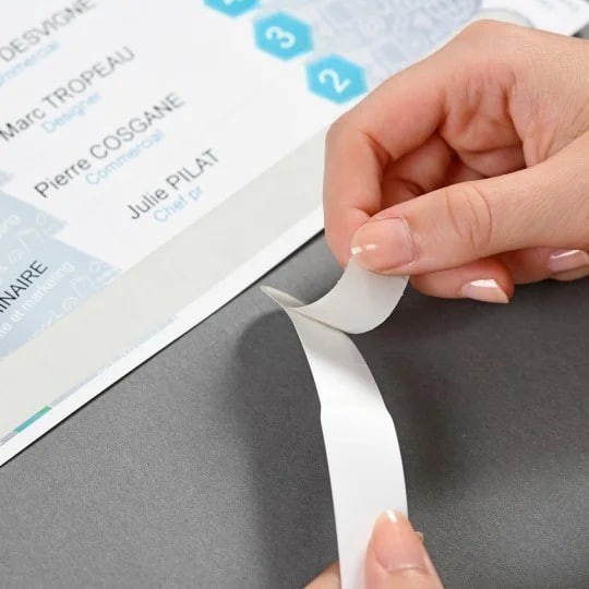 Krupni plan ruku koje odljepljuju samoljepljivi dio identifikacijske narukvice s lista papira.