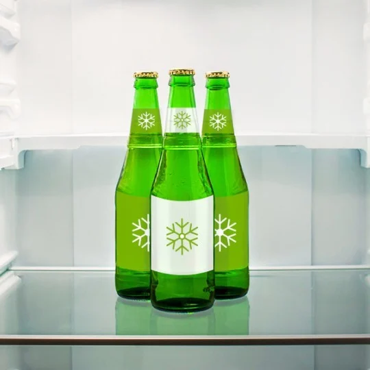 Tri zelene boce hladnog piva s etiketama sa snježnom pahuljom stoje na polici u otvorenom hladnjaku.