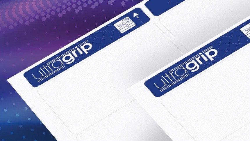 Povećani prikaz bijelih listova naljepnica Avery s plavom trakom UltraGrip na gornjem rubu. Na traci se vidi bijeli natpis ‘ultragrip’ na podlozi s romboidnim uzorkom te mala ikona omotnice. Pozadina grafike je ljubičasto‑plavi gradijent s točkicama.