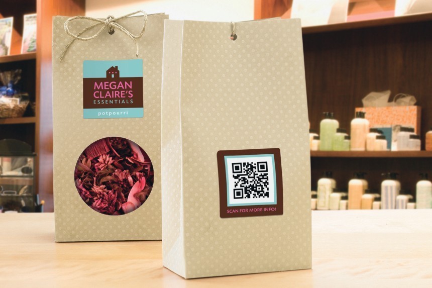 Dvije papirnate vrećice za potpourri. Na prednjoj vrećici vidljiva je naljepnica proizvoda "Megan Claire's Essentials", a na stražnjoj naljepnica s QR kodom, što demonstrira upotrebu naljepnica za brendiranje i interakciju s kupcima.