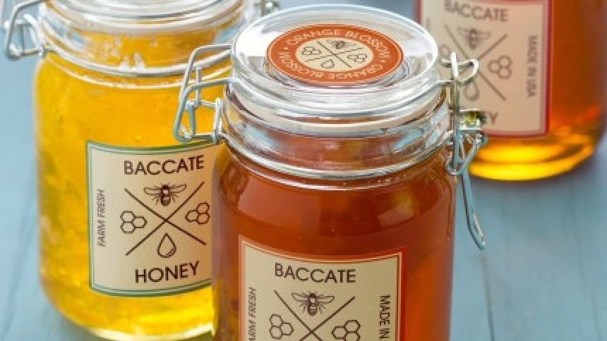 Dvije staklene staklenke meda s etiketama "Baccate Honey", prikazujući kako etikete izgledaju na ambalaži zanatskih proizvoda.