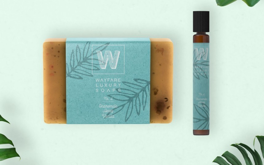 Pogled odozgo na pločicu sapuna s medom i roll-on parfem marke "Wayfare Luxury Soaps". Proizvodi su omotani tirkiznim etiketama s motivom lišća.