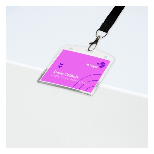 Slika prikazuje identifikacijsku oznaku na bijeloj površini. Oznaka je ružičasta s imenom 'Lucie Delbois' i titulom 'DIREKTORICA MARKETINGA'. Ima kopču pričvršćenu na crnu traku.