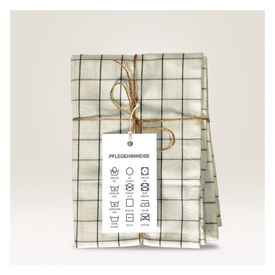 Slika prikazuje presavijenu tkaninu s kariranim uzorkom, zavezanu špagom. Uključuje etiketu s uputama za njegu koja sadrži različite simbole za pranje na njemačkom jeziku.
