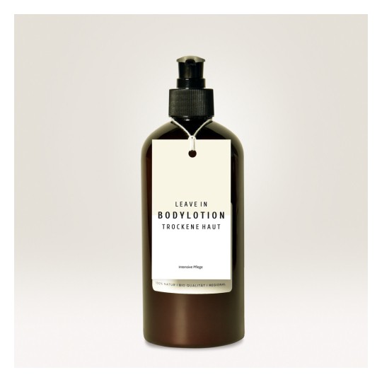 Slika prikazuje tamnosmeđu bočicu losiona za tijelo s etiketom na kojoj piše 'LEAVE IN BODYLOTION TROCKENE HAUT' i 'Intensive Pflege'. Bočica ima pumpicu na vrhu i minimalistički dizajn.