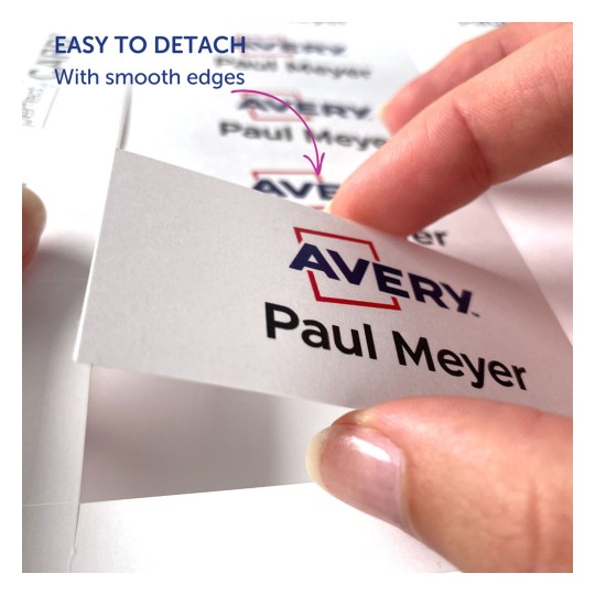 Slika prikazuje ruku koja drži oznaku s imenom 'Avery Paul Meyer.' Ističe lakoću odvajanja oznake, naglašavajući glatke rubove.
