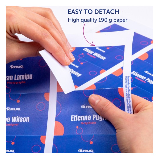 Slika prikazuje ruke koje odvajaju dio visokokvalitetnog otisnutog papira na kojem su prikazana imena i uloge. Pozadina ima živopisan dizajn s plavim i crvenim elementima.