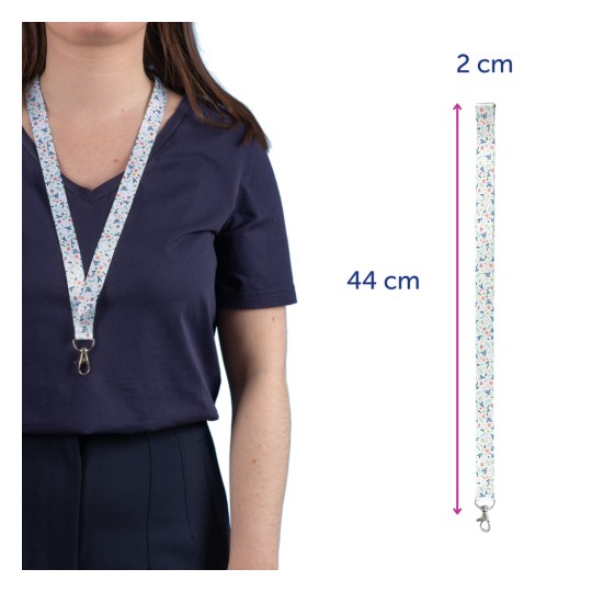 Slika prikazuje osobu koja nosi uzicu s cvjetnim uzorkom oko vrata. Uzica je dugačka 44 cm i široka 2 cm, dizajnirana za držanje predmeta kao što su ključevi ili bedževi.