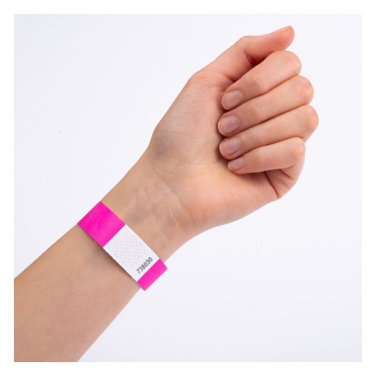 Slika prikazuje ruku s ružičastom narukvicom koja ima bijelu oznaku i otisnut broj. Ruka je postavljena s prstima skupljenima, a narukvica je jasno vidljiva.