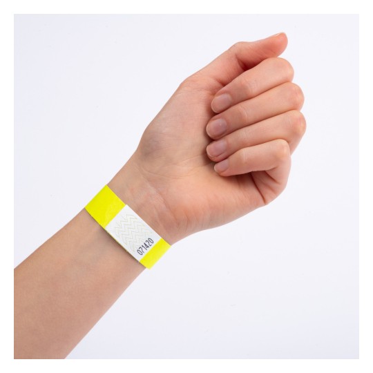 Ova slika prikazuje ruku s žutom narukvicom koja ima bijeli dio sa cik-cak uzorkom i brojem na njemu.