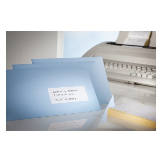 Slika prikazuje skupinu plavih kuverti s oznakom adrese. U pozadini je vidljiv printer uz hrpu praznih naljepnica.