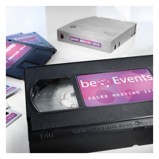 Slika sadrži VHS kazetu s naljepnicom 'beEvents SALES MEETING 2014' uz druge uređaje za pohranu medija, kao što su diskete i podatkovna kaseta, svi sličnog brendiranja.