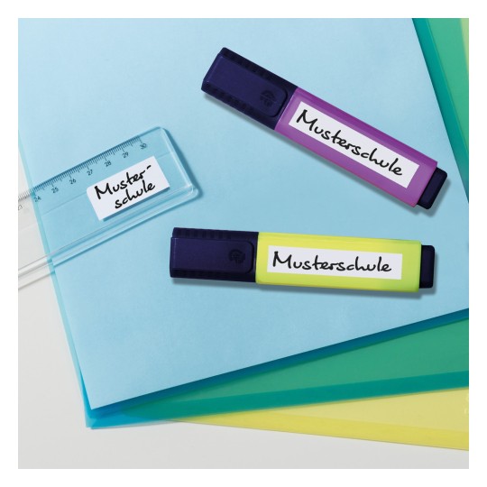Slika prikazuje dva markera označena kao 'Mustersschule' i prozirno ravnalo na plavoj pozadini s nekoliko listova obojenog papira.