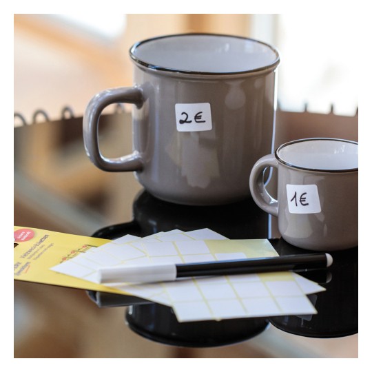 Slika prikazuje dvije keramičke šalice na crnoj površini. Veća šalica košta 2€, a manja 1€. Pored njih su također listovi s etiketama i crna olovka.