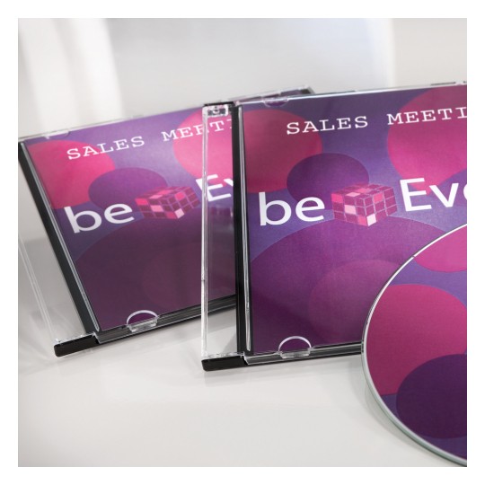 Slika prikazuje dvije kutije za CD s naslovom 'Sales Meeting' i disk s raznobojnim dizajnom. Dizajn uključuje krugove u nijansama ružičaste i ljubičaste boje, zajedno s tekstom 'beEven.'