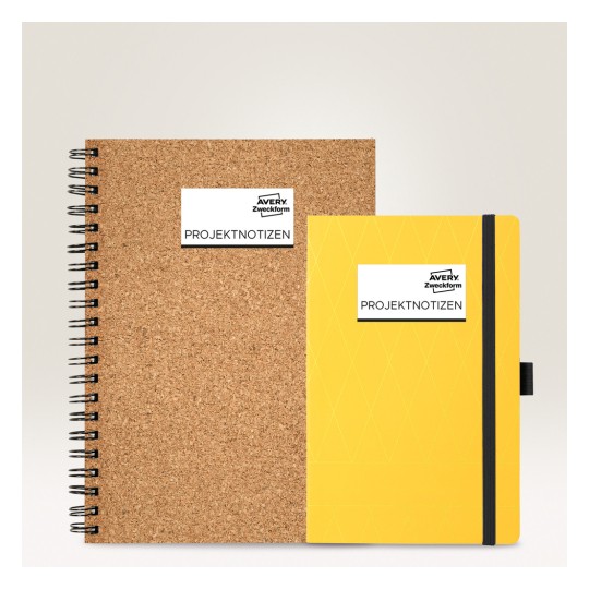 Slika prikazuje dvije bilježnice: jedna je spiralna bilježnica od pluta, a druga je žuta bilježnica s remenom, obje označene s 'PROJEKTNOTIZEN' i marke 'Avery Zweckform'.