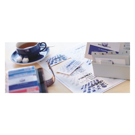 Slika prikazuje šalicu čaja pored kolekcije posjetnica i tiskovina, uključujući bijelu mapu i razne dizajne posjetnica. Ispod je svijetla drvena površina stola.