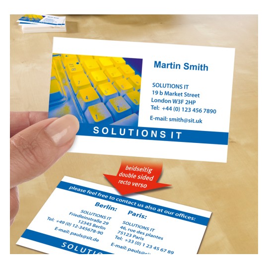 Slika prikazuje posjetnicu držanu između prstiju, s kontaktnim podacima i informacijama s obje strane za tvrtku nazvanu 'SOLUTIONS IT'. U pozadini je djelomično vidljiva šarena tipkovnica.