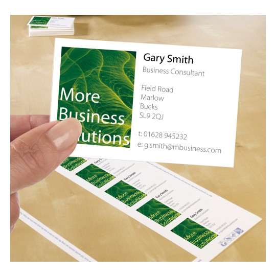 Slika prikazuje posjetnicu s imenom, kontaktnim podacima i dizajnom s zelenim uzorcima. Ruka drži jednu karticu, dok su ostale kartice vidljive u hrpi na stolu.