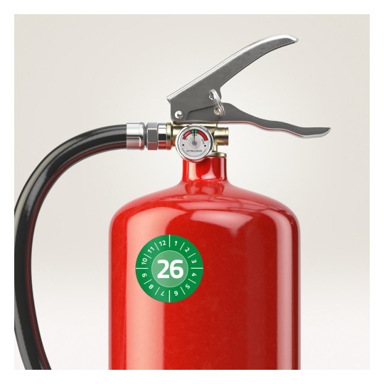 Slika prikazuje krupni plan crvenog vatrogasnog aparata. Aparat ima ručku i mlaznicu, kao i manometar na vrhu koji pokazuje status. Na tijelu se nalazi zelena kružna naljepnica s brojem 26.