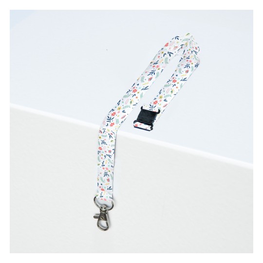 Slika prikazuje uzorčanu vrpcu s cvjetnim motivima i metalnom kopčom, položenu na svijetlu površinu.